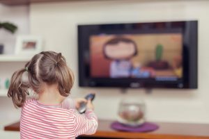  A child sitting alone on a sofa, engaged in screen time, watching cartoons on a television