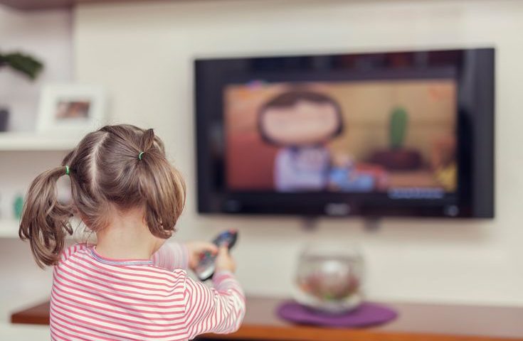 A child sitting alone on a sofa, engaged in screen time, watching cartoons on a television