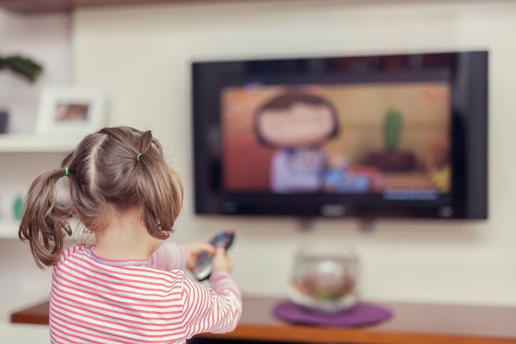 A child sitting alone on a sofa, engaged in screen time, watching cartoons on a television