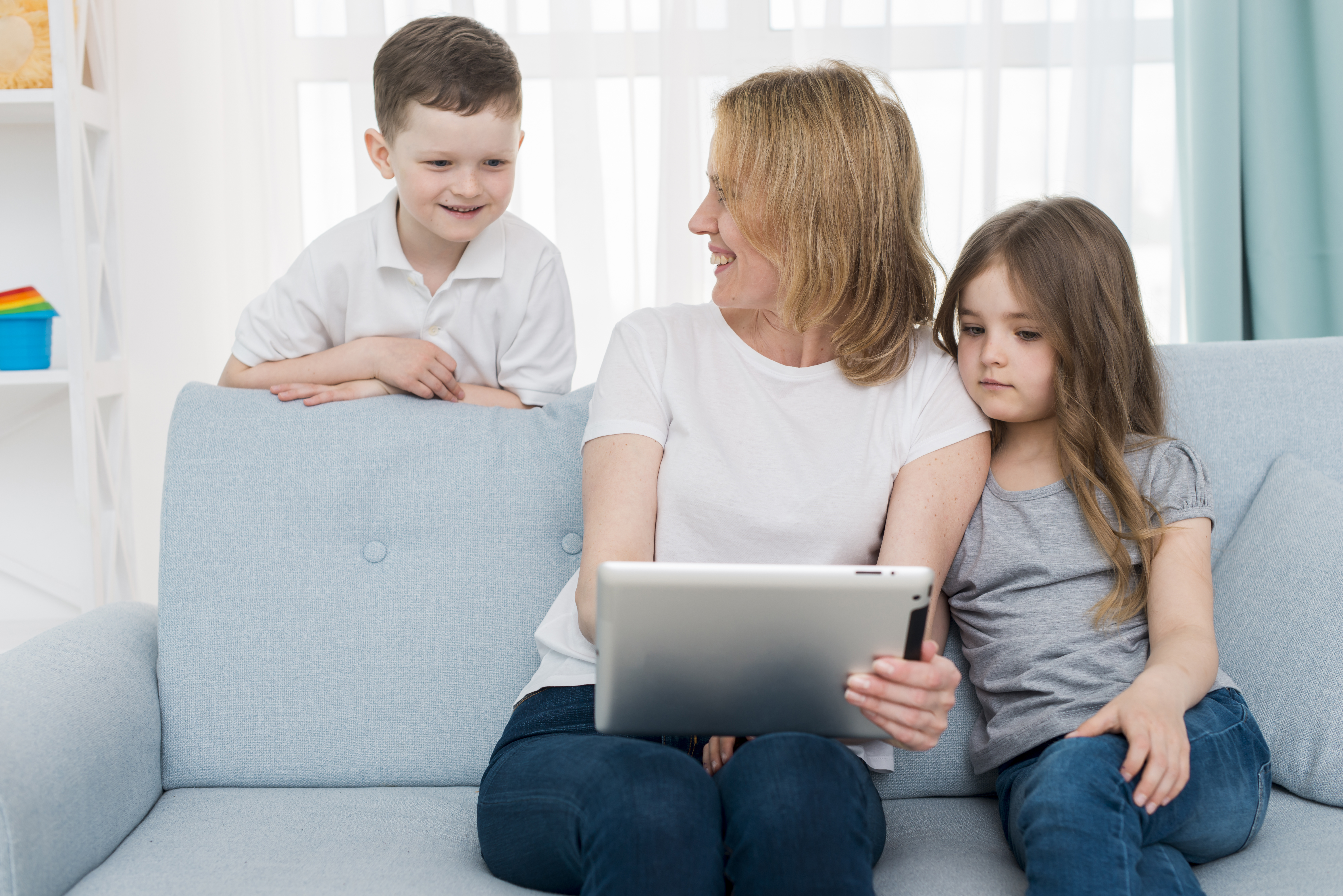 A mother holds a tablet device while her kids sits beside her, engaged in screen time activities together