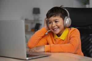 A child wearing headphones and sitting at a desk, using a laptop during screen time.