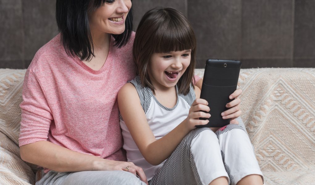 A child sits with their mother, both looking at a smartphone screen during screen time.