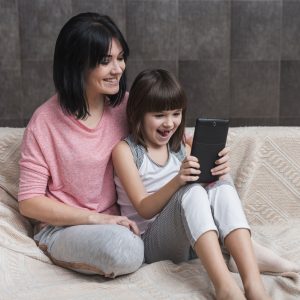 A child sits with their mother, both looking at a smartphone screen during screen time.