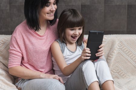 A child sits with their mother, both looking at a smartphone screen during screen time.