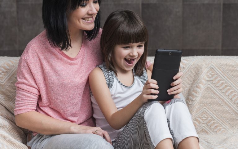 A child sits with their mother, both looking at a smartphone screen during screen time.