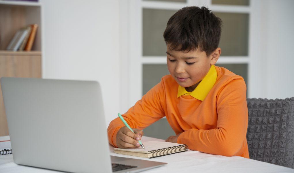 Screen Time: A young boy sits at a desk, focused on a laptop for educational screen activities- Babyhub