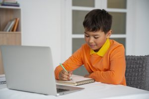 Screen Time: A young boy sits at a desk, focused on a laptop for educational screen activities- Babyhub